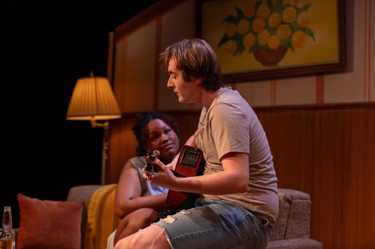 Tristan seated indoors playing guitar in The Legend of Georgia McBride